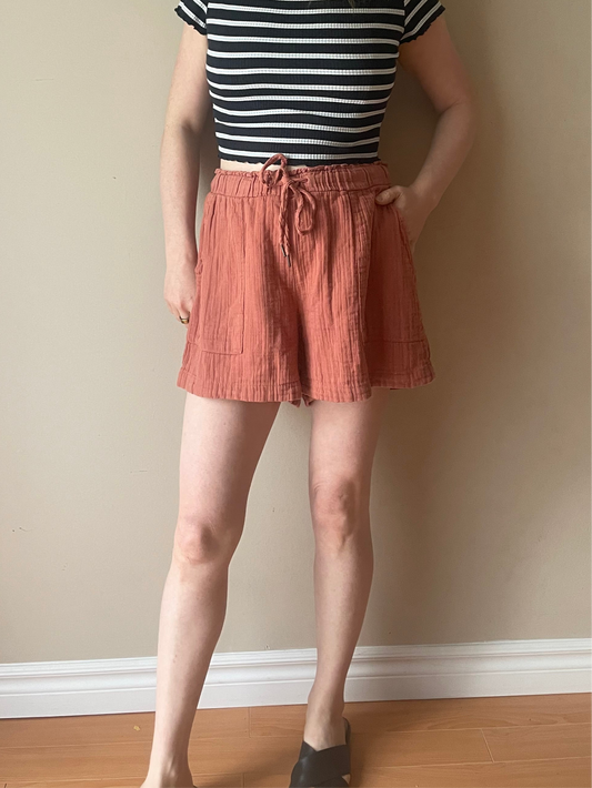 Woman wearing Gap rust textured cotton drawstring shorts with side patch pockets, styled with a navy striped crop top for a relaxed summer outfit.