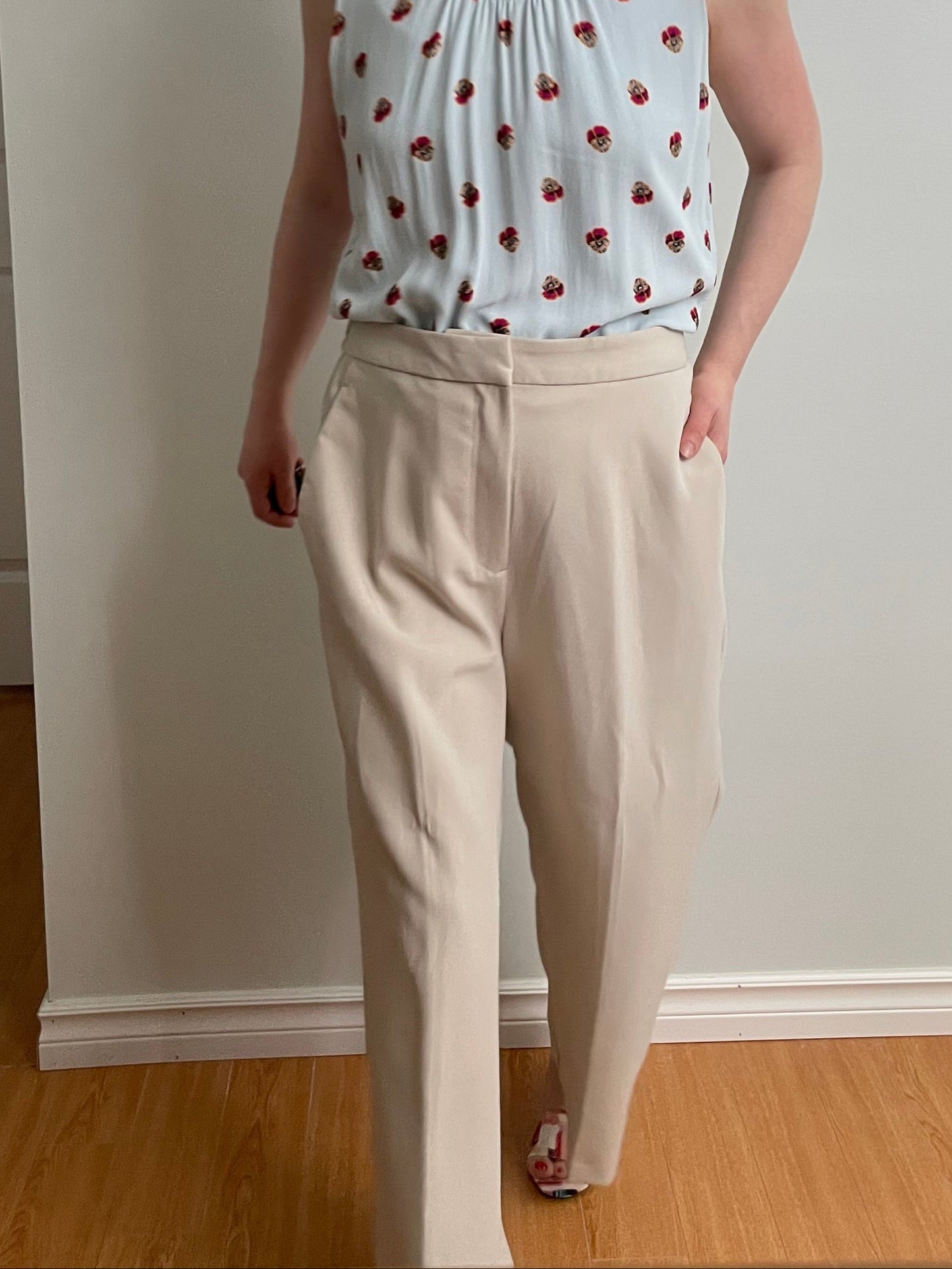 Person wearing a light blue sleeveless top with red patterns and beige pants indoors.