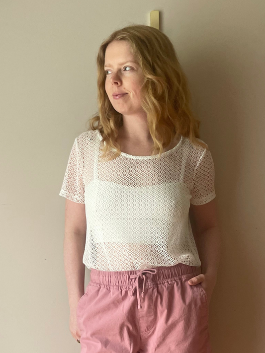 Woman wearing Gabby Isabella white open-knit short sleeve top layered over a white camisole, styled with mauve shorts for a light and casual summer outfit.