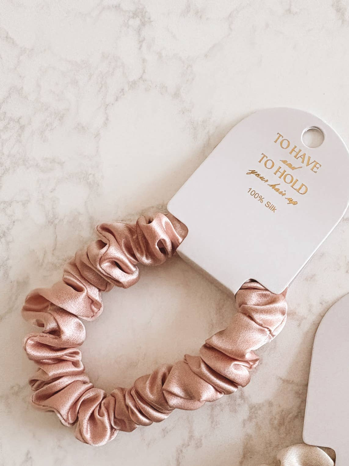 Two satin scrunchies on a marble surface with 'To Have & To Hold' packaging.