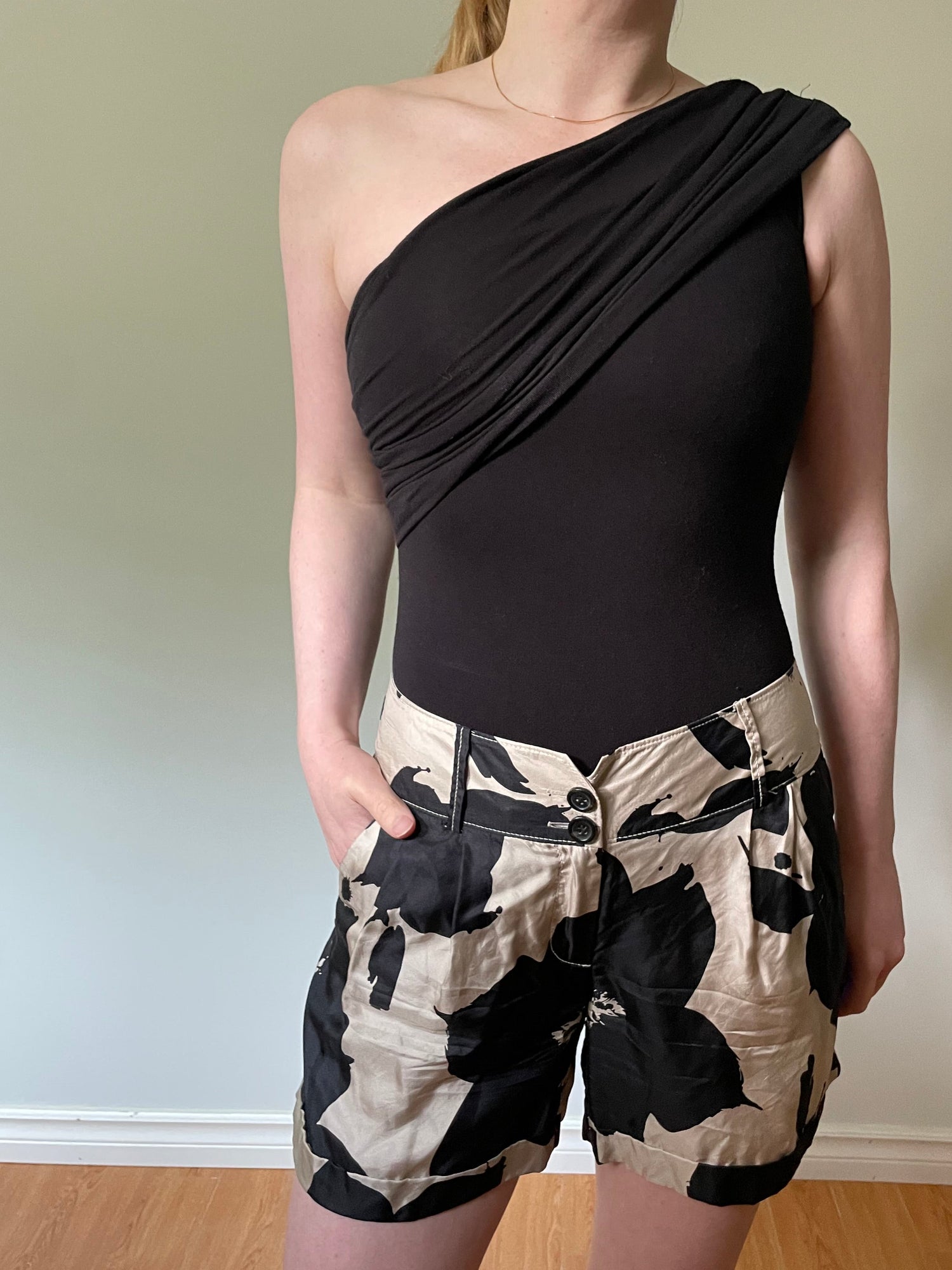 A woman wearing a black strapless tube top and black-and-beige floral print shorts, shown in a mirror selfie in an indoor room.