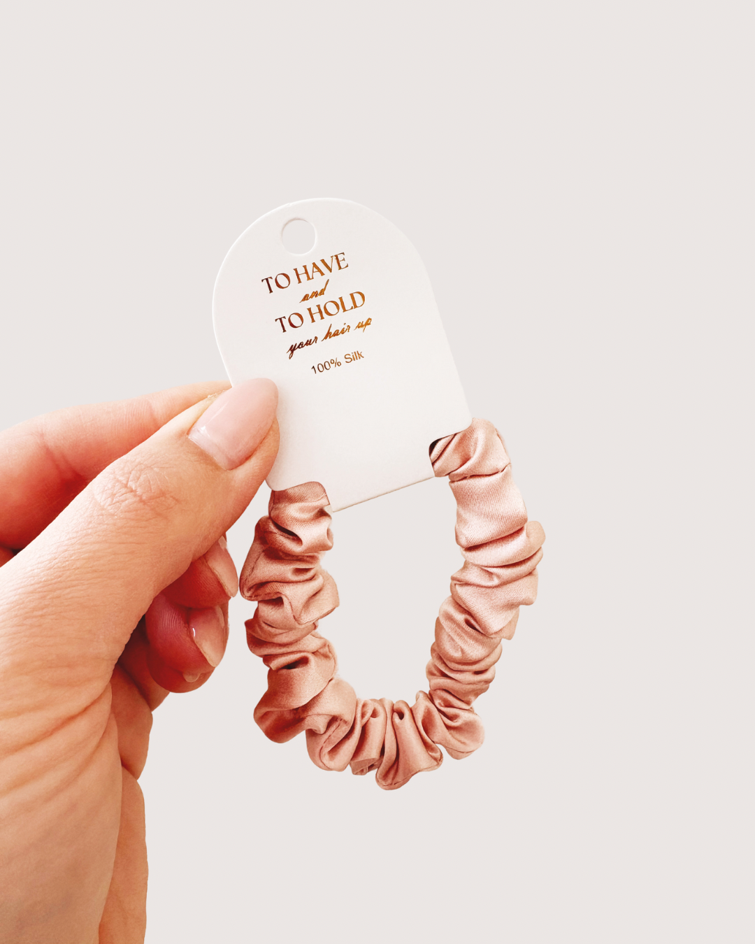 Pink scrunchie held by a hand with a white card in the background