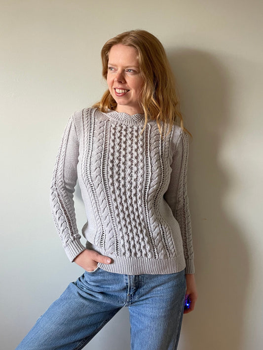 Person wearing a patterned sweater and blue jeans against a plain background