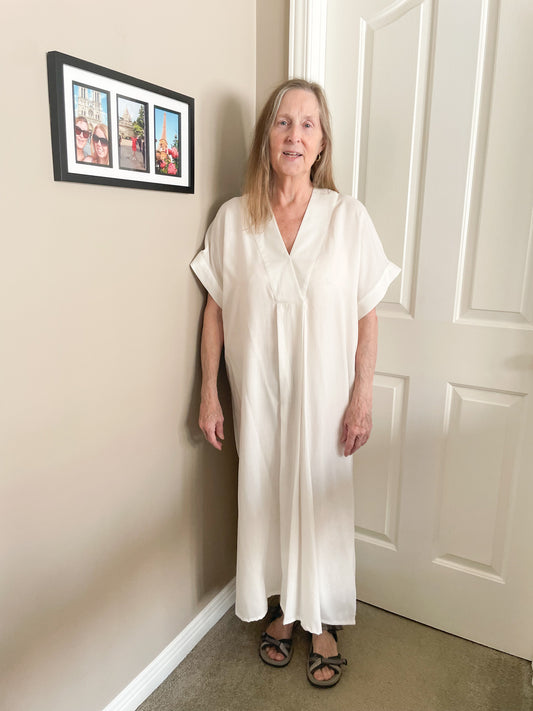 Woman wearing an off-white kaftan-style maxi dress with V-neck and side slits, made of textured Lyocell fabric.