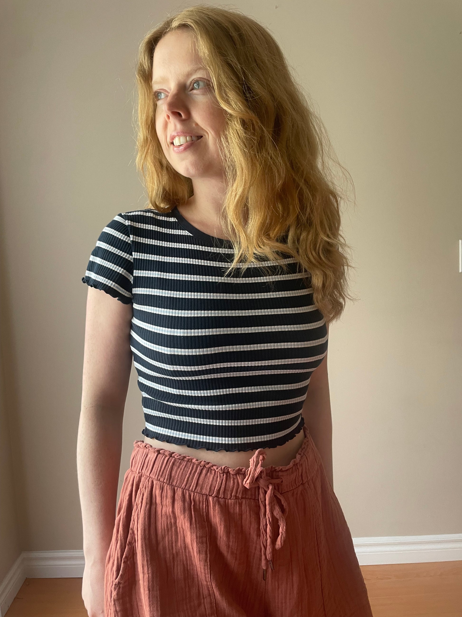 Woman wearing Uniqlo navy and white ribbed striped crop top with lettuce-edge hem, styled with rust drawstring shorts for a casual summer look.